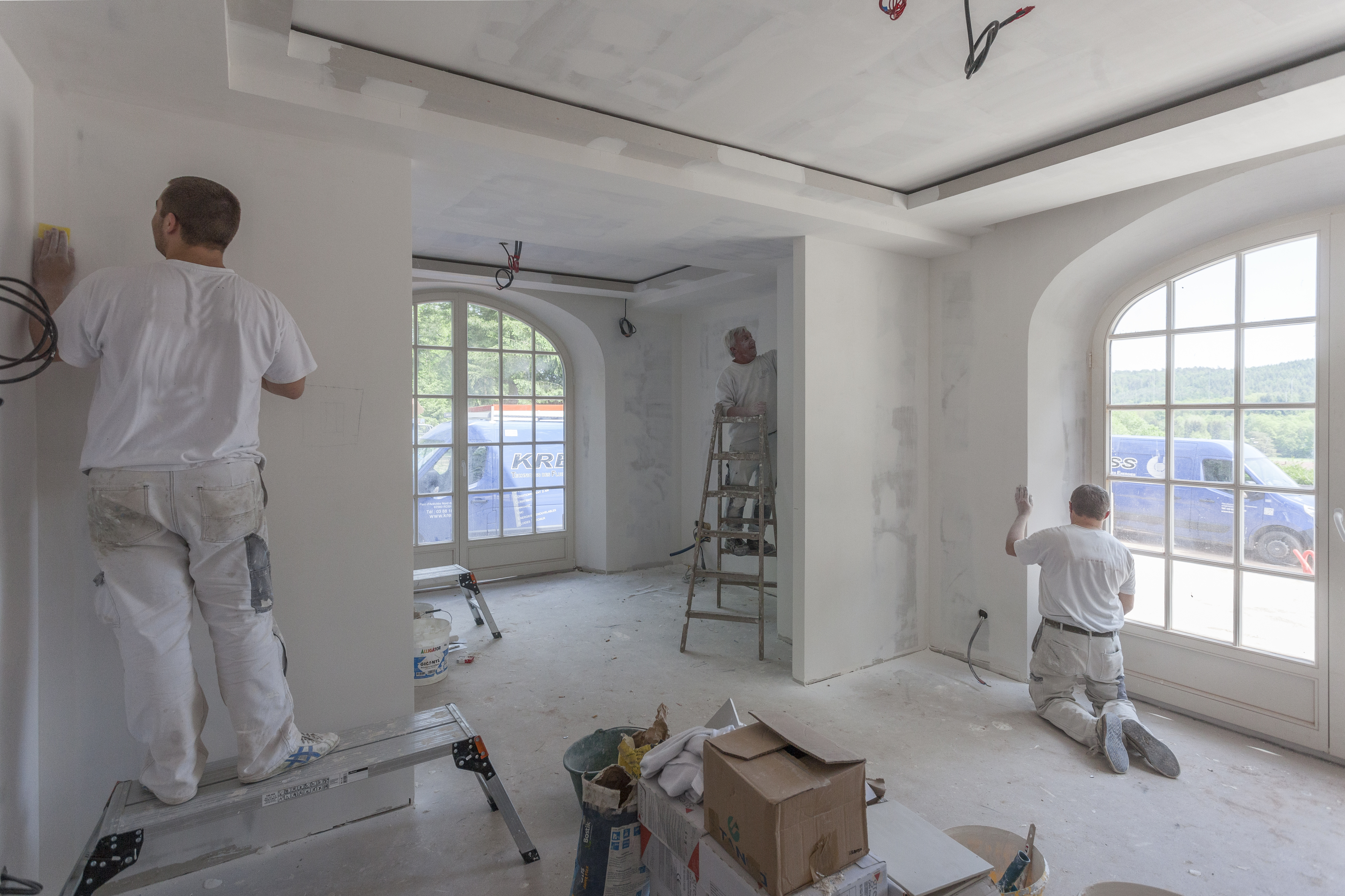 Trois ouvriers en train de peindre les murs d'une pièce dans un chantier.